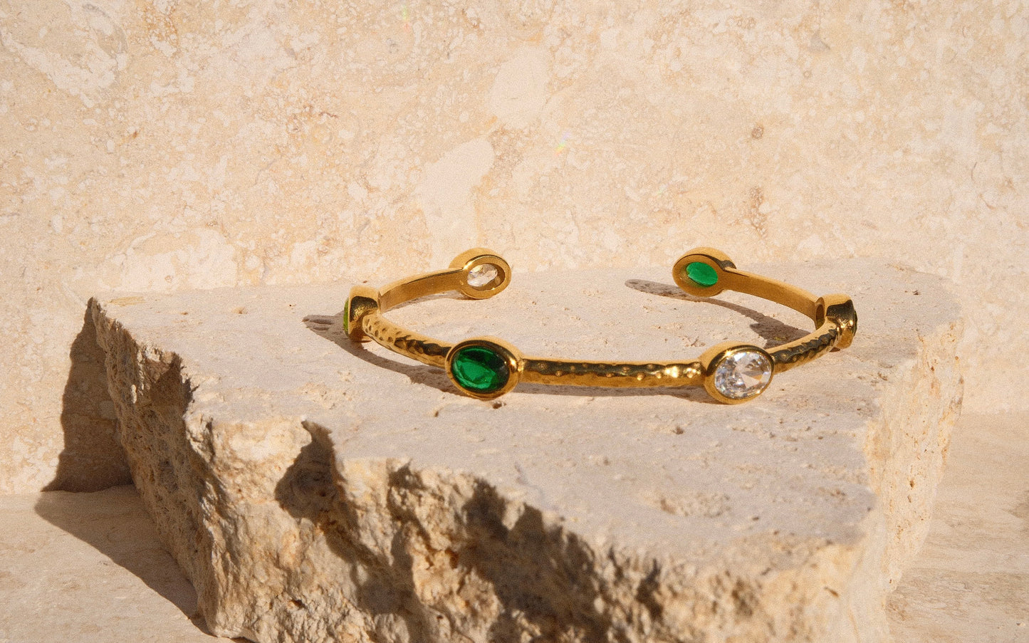 Gold bracelet with green gemstones on a stone surface