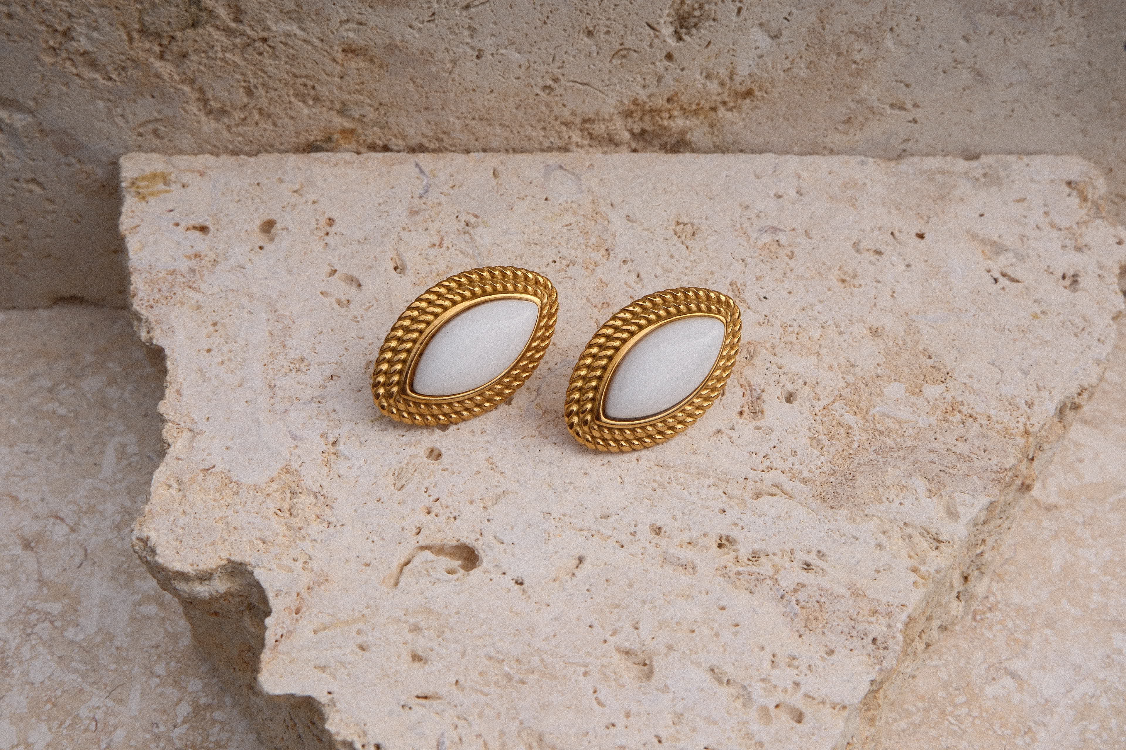 Pair of gold earrings with white stones on a textured stone surface