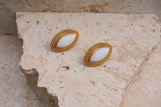 Pair of gold earrings with white stones on a textured stone surface
