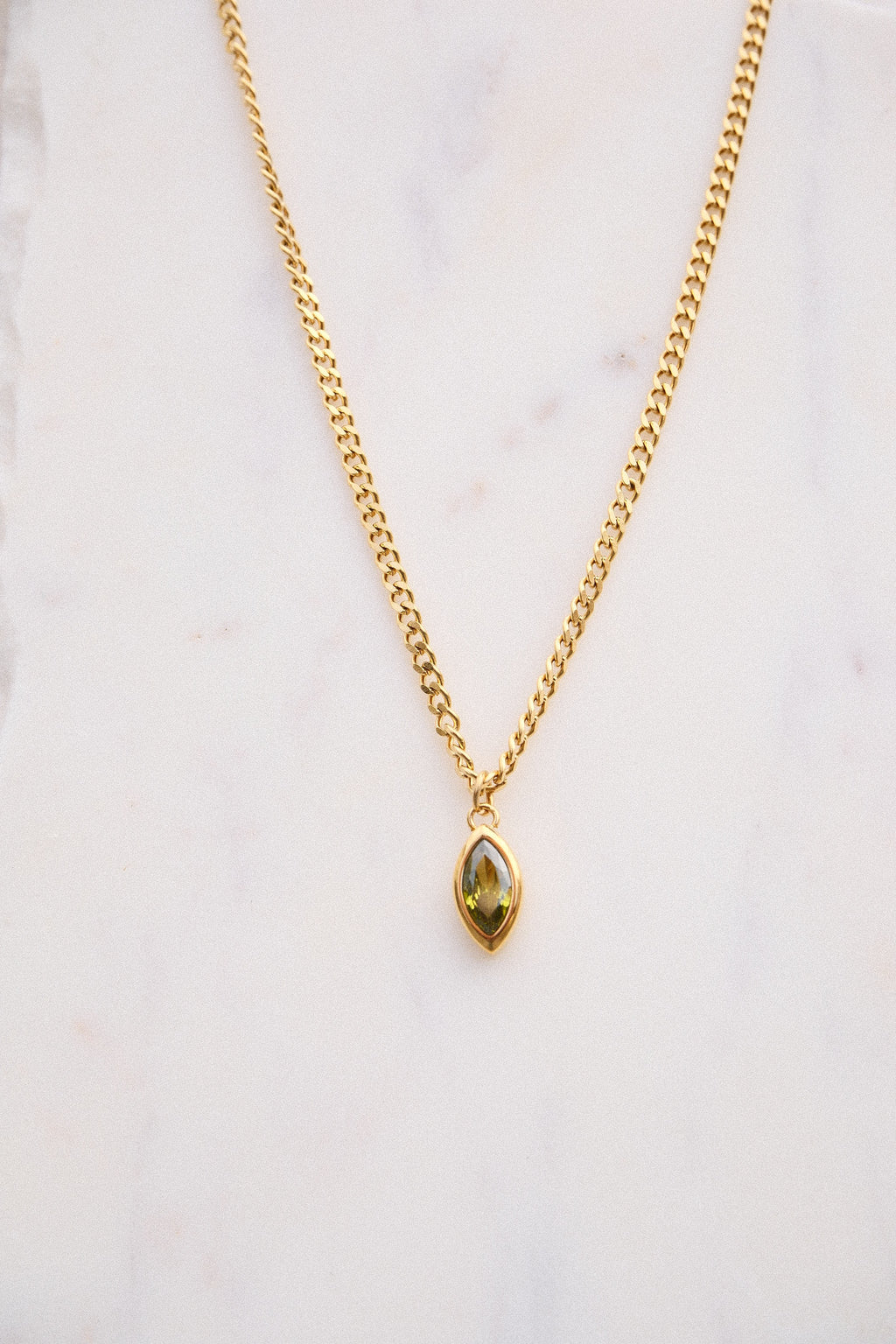 Gold necklace with a green gemstone pendant on a light background