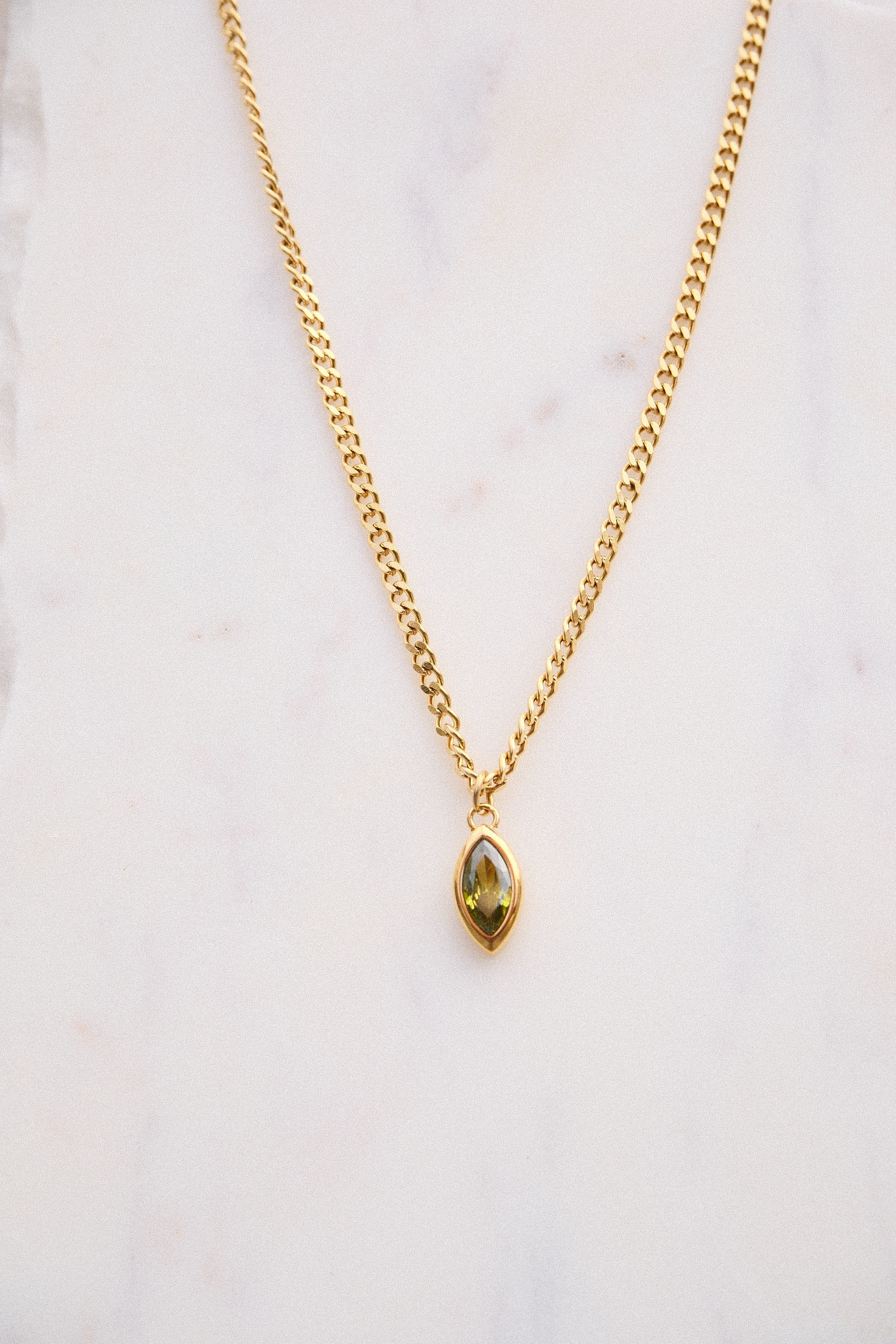 Gold necklace with a green gemstone pendant on a light background