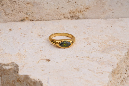 Gold ring with a green stone on a textured stone surface
