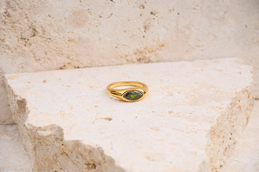 Gold ring with a green gemstone on a textured stone surface