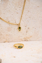 Gold ring and necklace with green gemstones on a textured beige surface