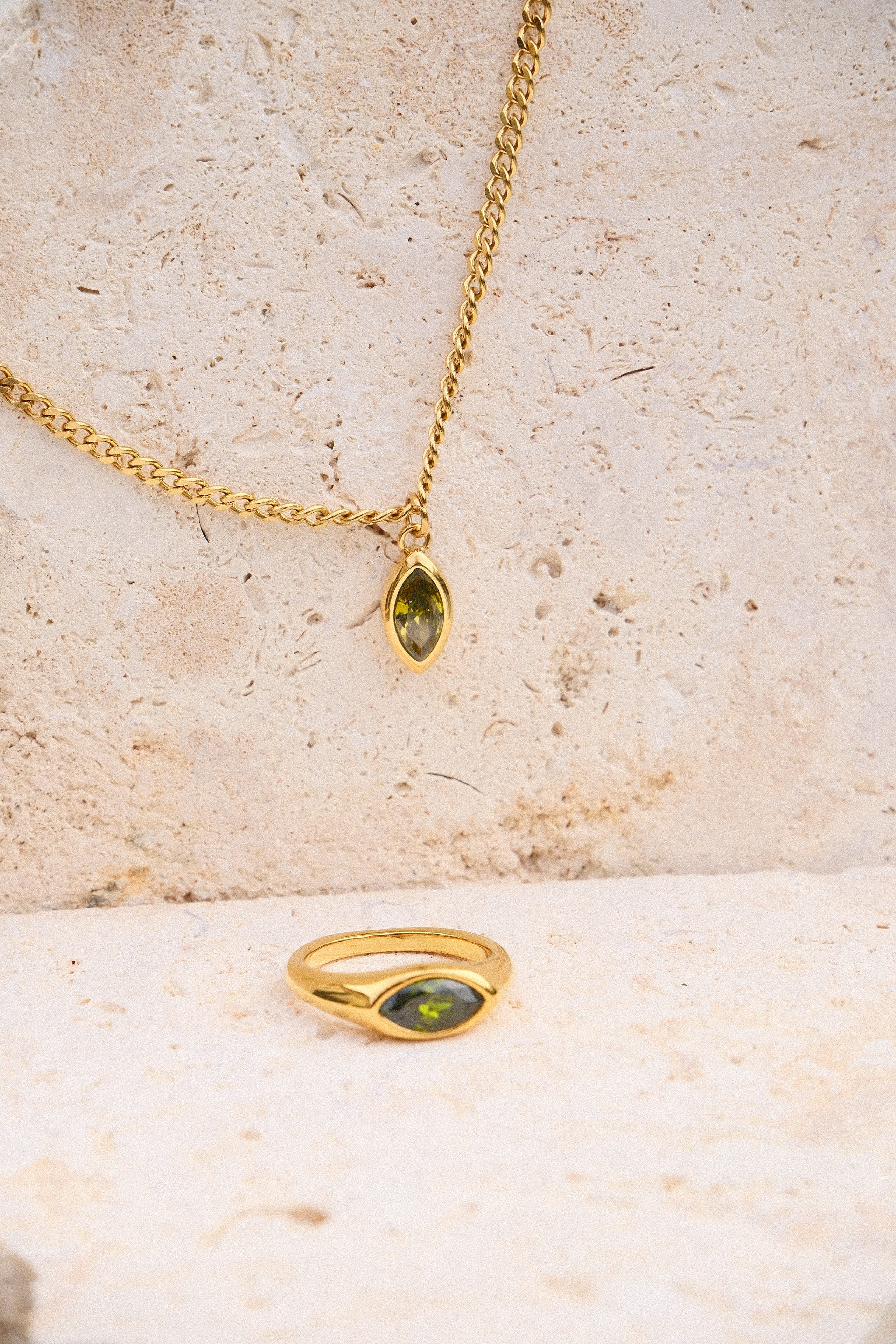 Gold ring and necklace with green gemstones on a textured beige surface