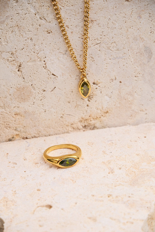 Gold ring and necklace with green gemstones on a textured beige surface