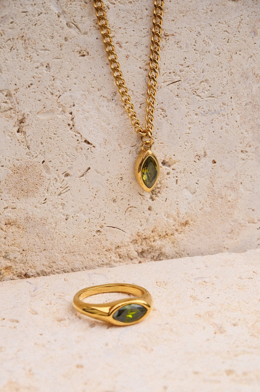 Gold ring and necklace with green gemstones on a textured stone surface