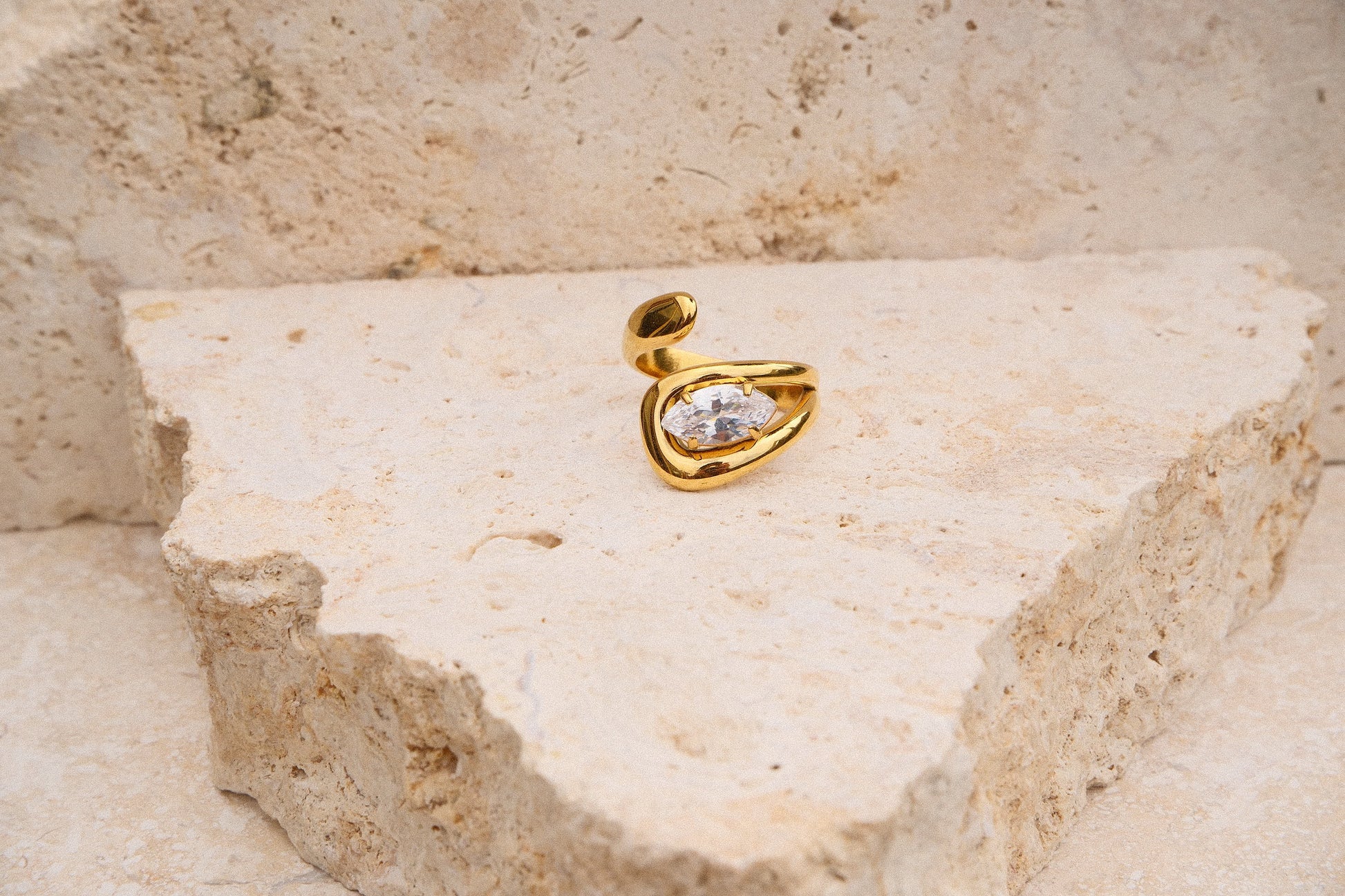 Gold ring with a marquise gemstone on a textured beige stone surface