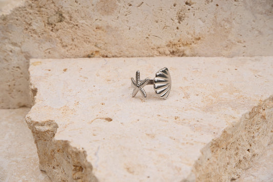 Silver starfish-shaped earring on a textured stone surface