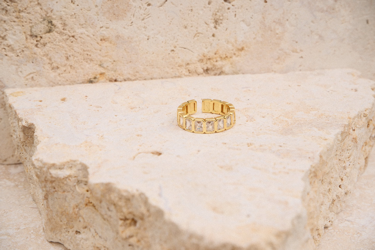 Gold ring with embedded stones on a textured beige surface
