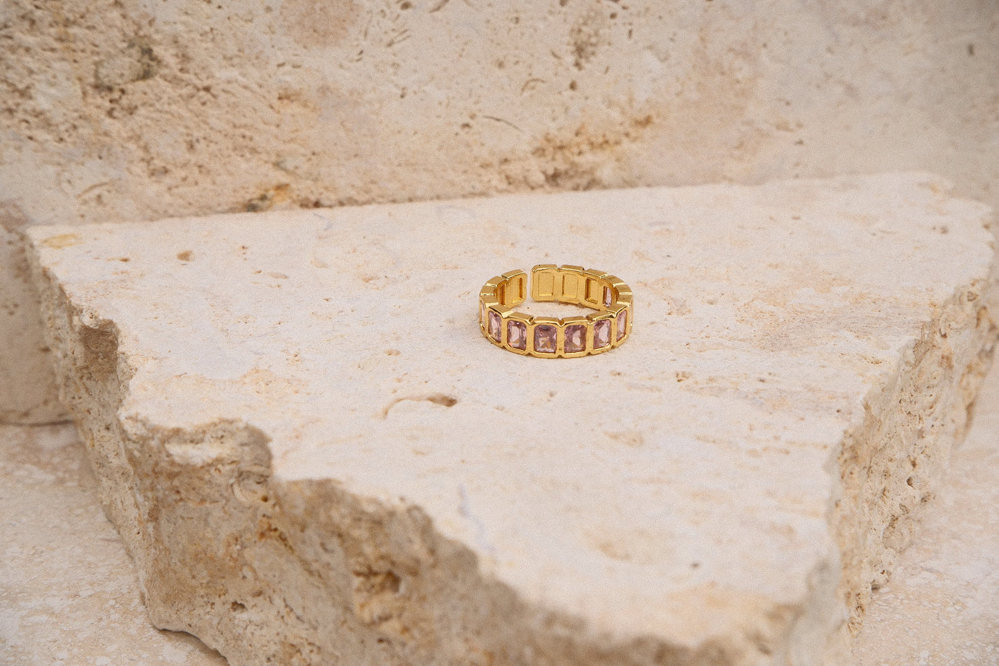 Gold ring with pink stones on a textured stone surface