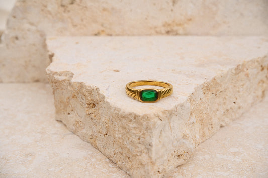 Gold ring with a green gemstone on a textured stone surface