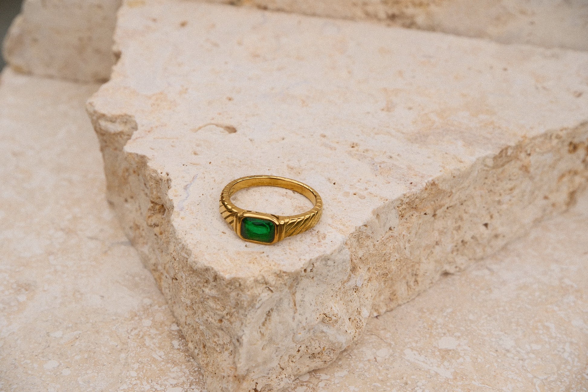 Gold ring with a green gemstone on a textured stone surface