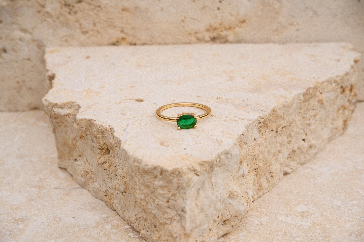 Gold ring with a green gemstone on a textured stone surface