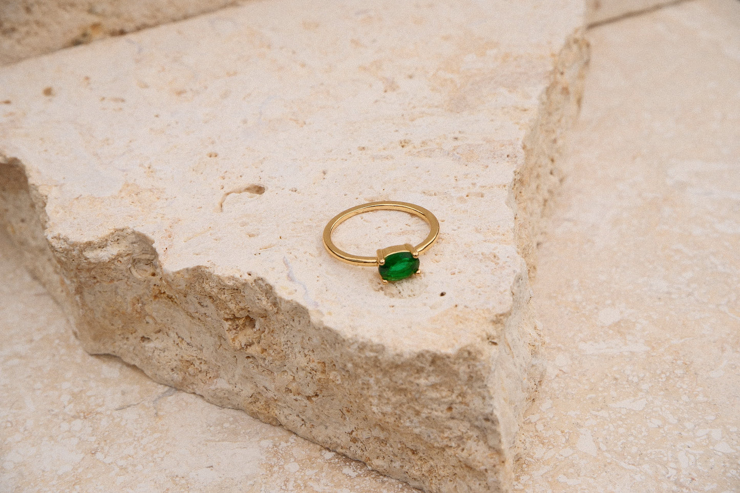 Gold ring with a green gemstone on a textured stone surface