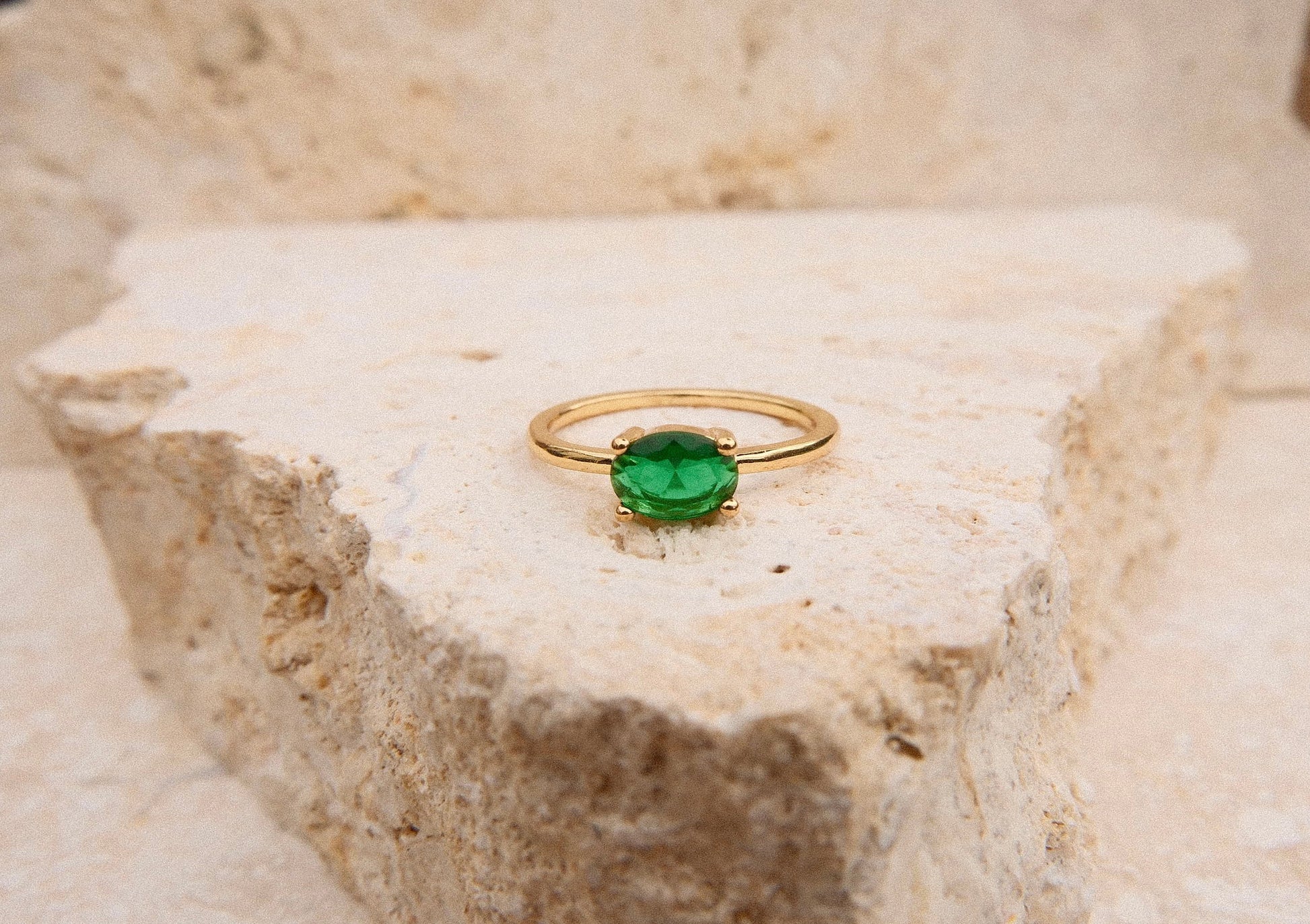 Gold ring with a green gemstone on a textured stone surface