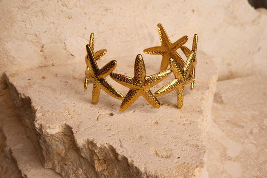 Gold starfish-shaped bracelet on a textured beige surface