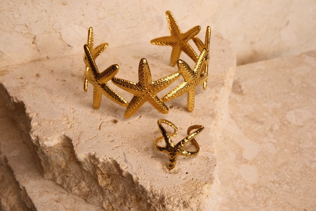 Gold starfish-shaped bangle and ring on a textured stone surface