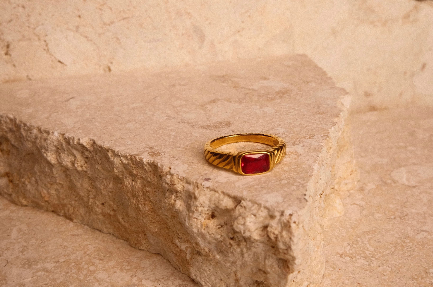 Gold ring with a red stone on a textured beige surface
