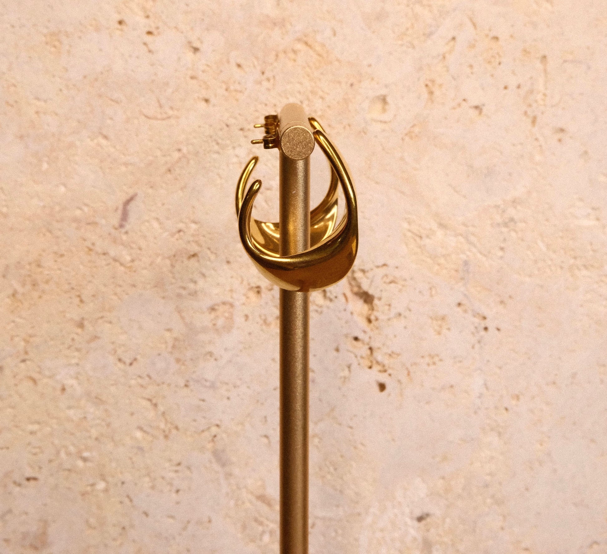 Gold earrings on a beige stone background