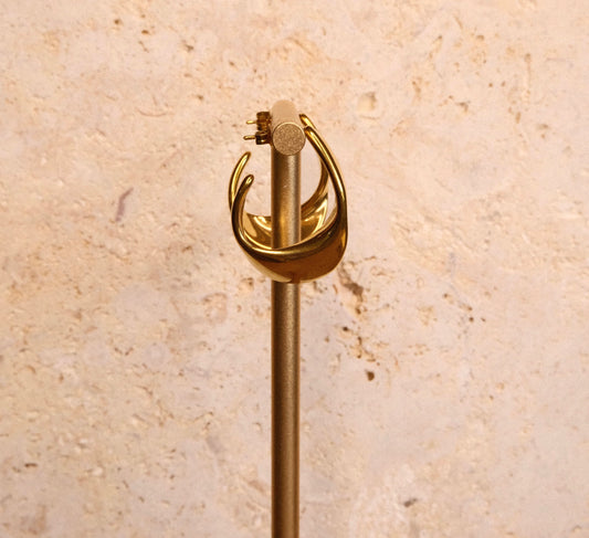 Gold earrings on a beige stone background