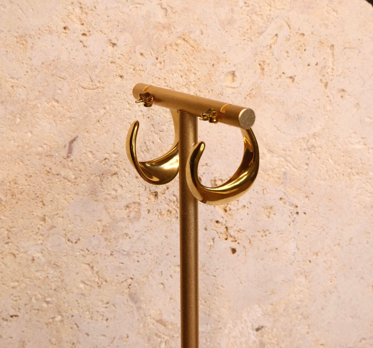 Gold earrings on a beige stone background
