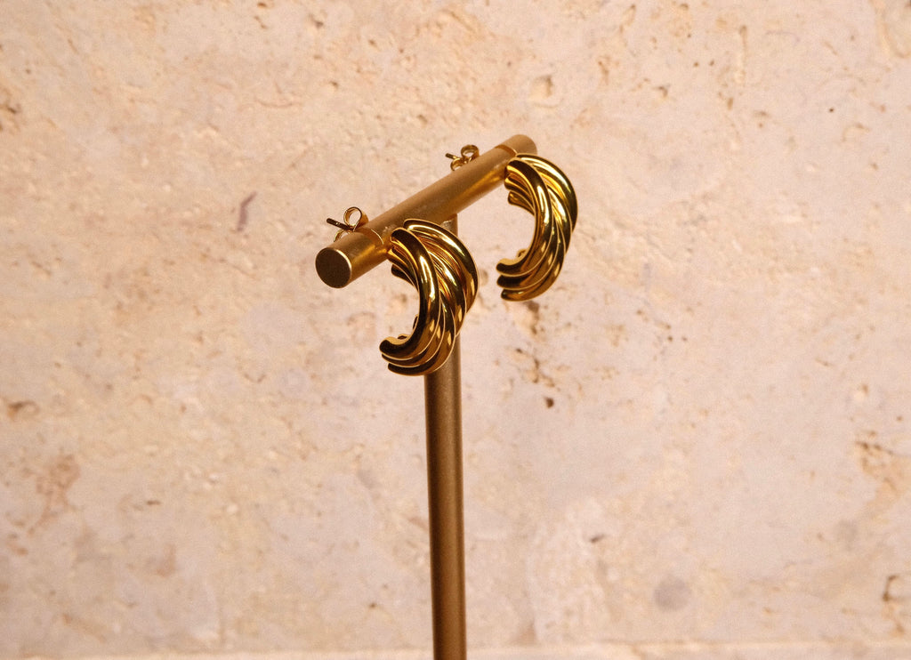 Gold earrings on stand against a beige marble background
