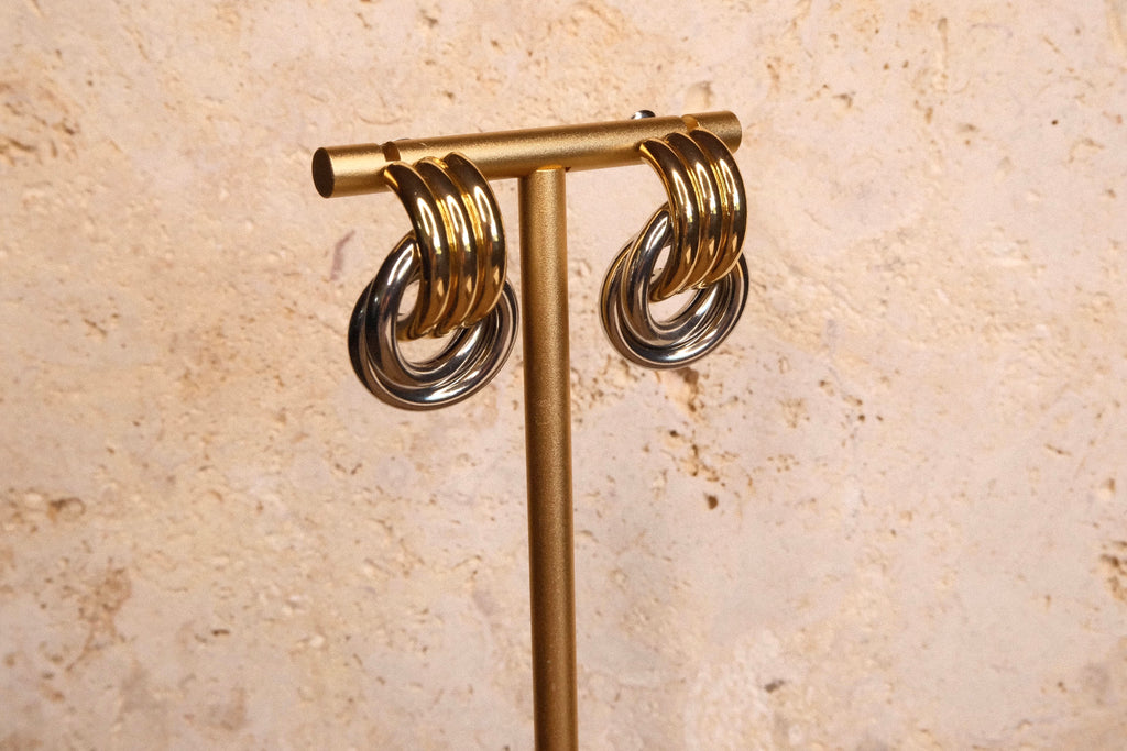 Gold and silver hoop earrings on a gold T-shaped stand against a beige stone background