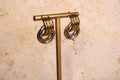 Gold and silver hoop earrings on a gold T-shaped stand against a beige stone background