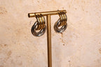 Gold and silver hoop earrings on a gold T-shaped stand against a beige stone background
