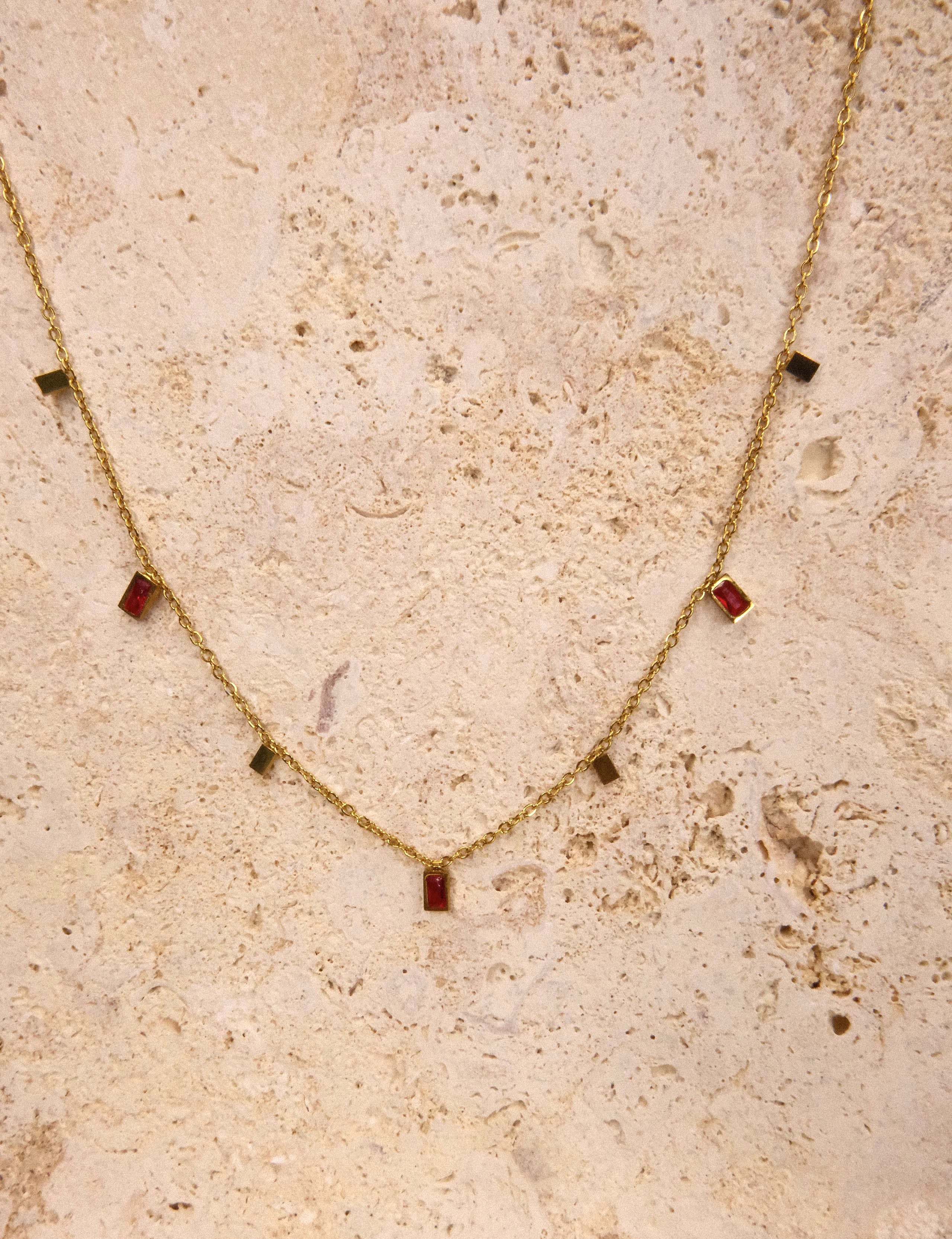 Gold necklace with red gemstones on a textured beige surface