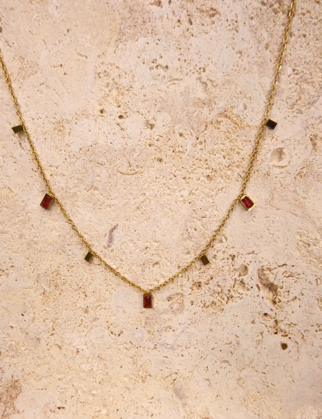 Gold necklace with red gemstones on a textured beige surface