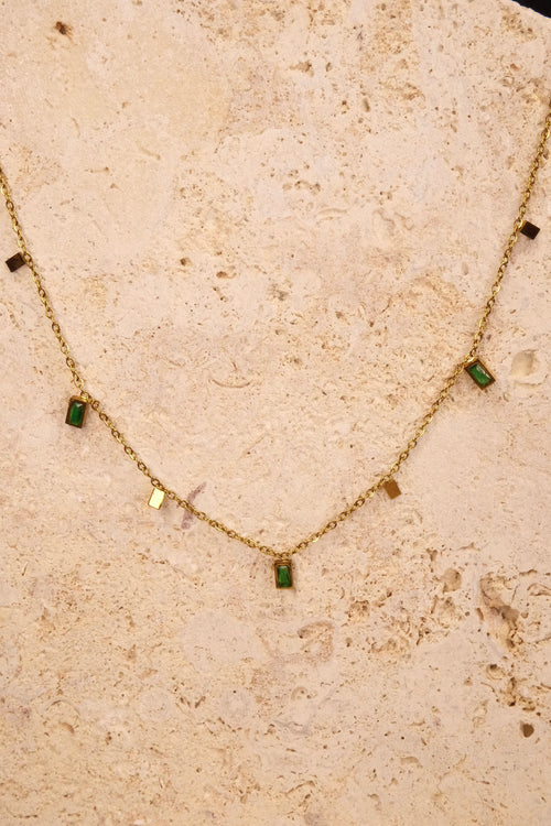 Gold necklace with green gemstones on a beige stone surface