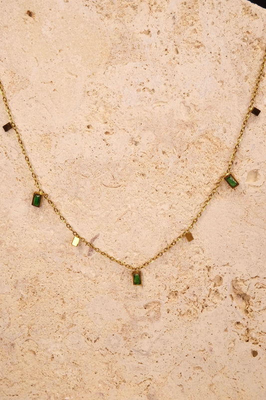 Gold necklace with green gemstones on a beige stone surface