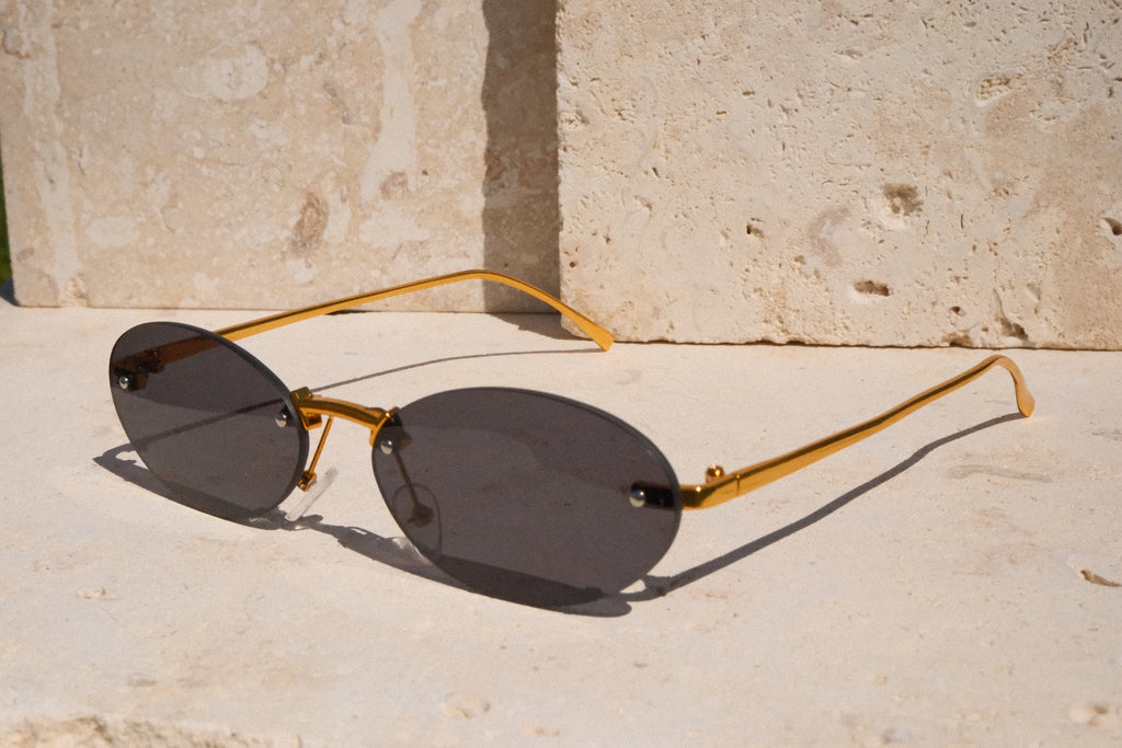 Gold-framed sunglasses with dark lenses on a stone surface