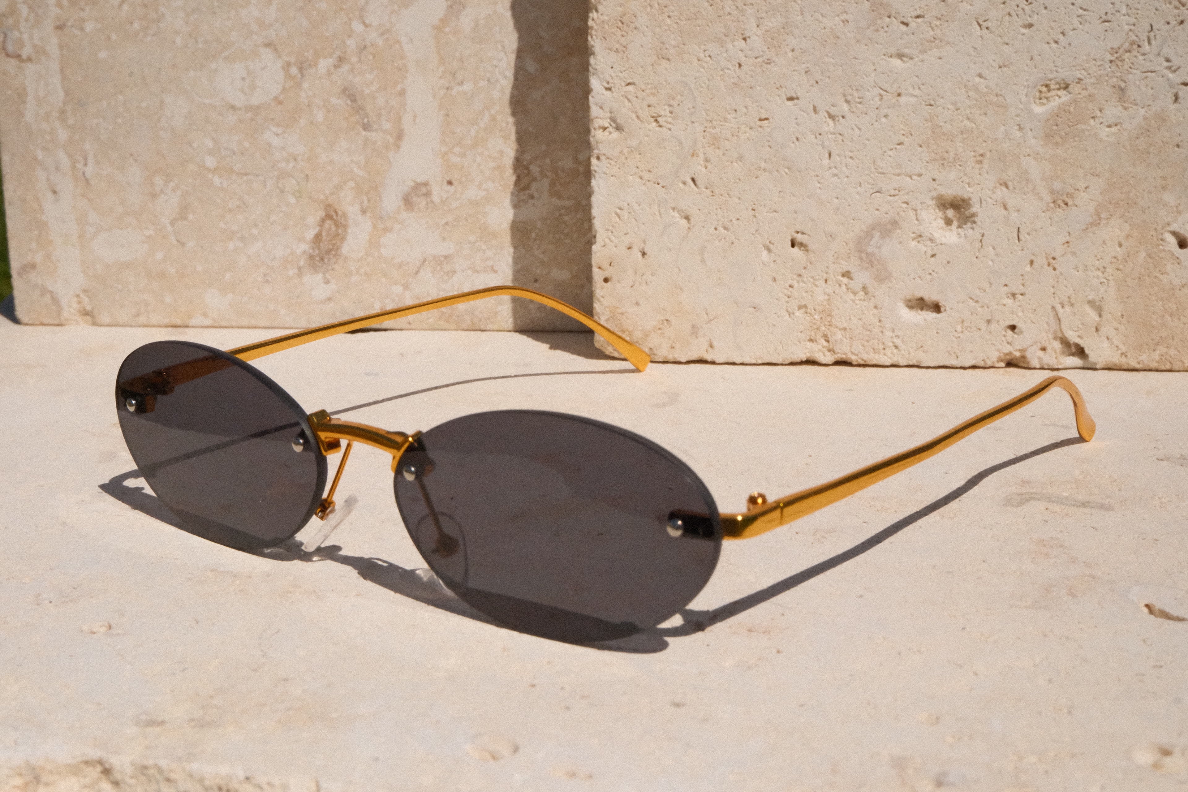 Gold-framed sunglasses with dark lenses on a stone surface