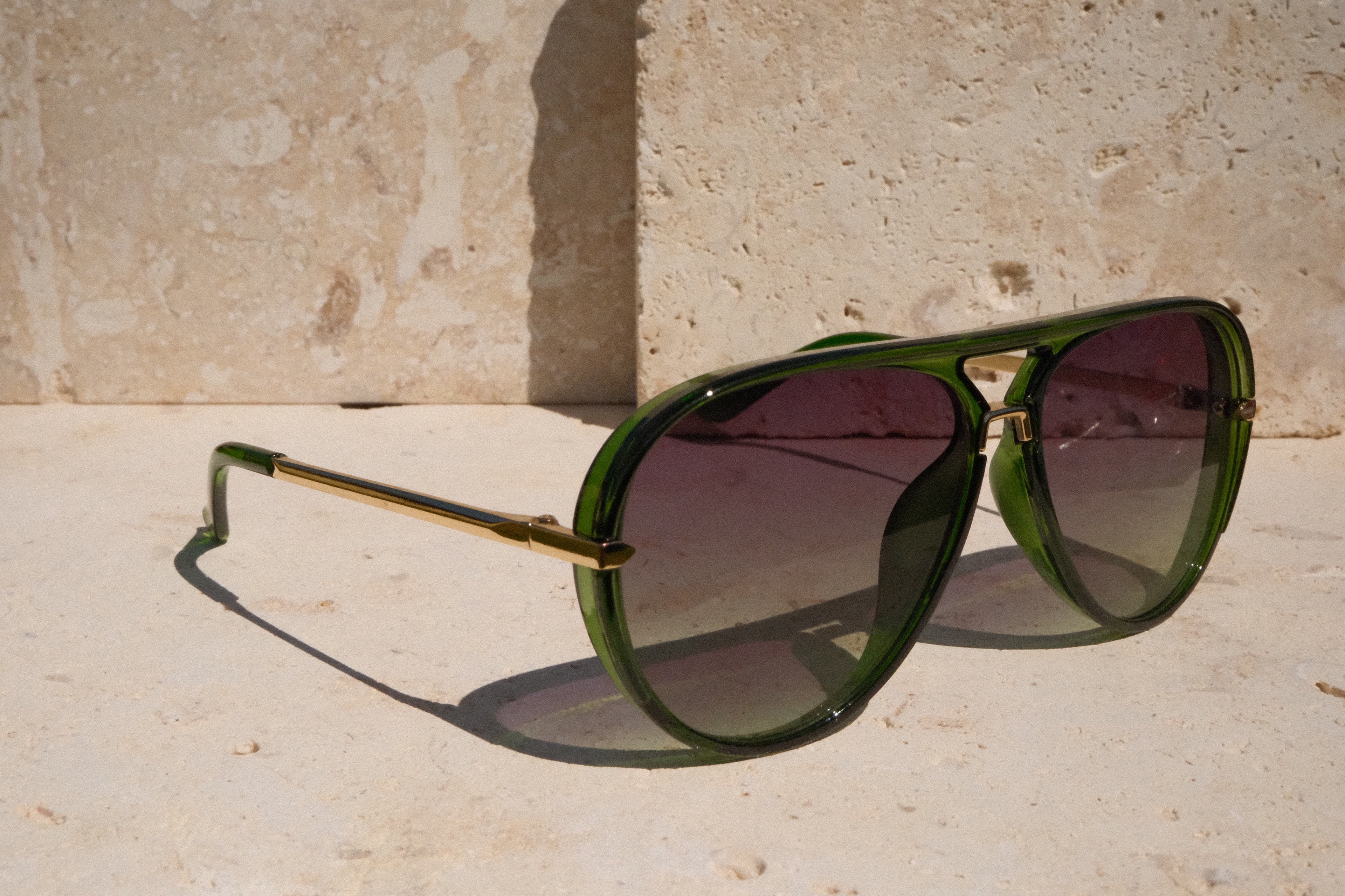 Green sunglasses with gold frame on a stone surface
