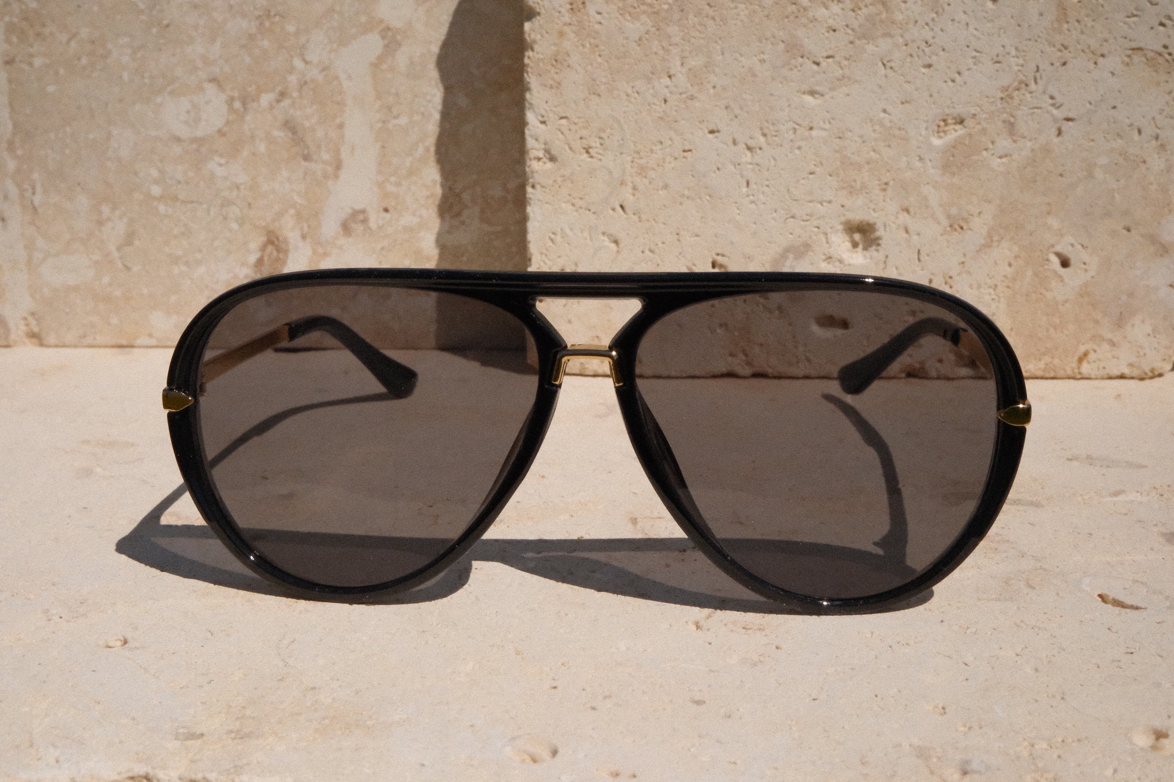 Black aviator sunglasses on a stone surface with a stone wall background