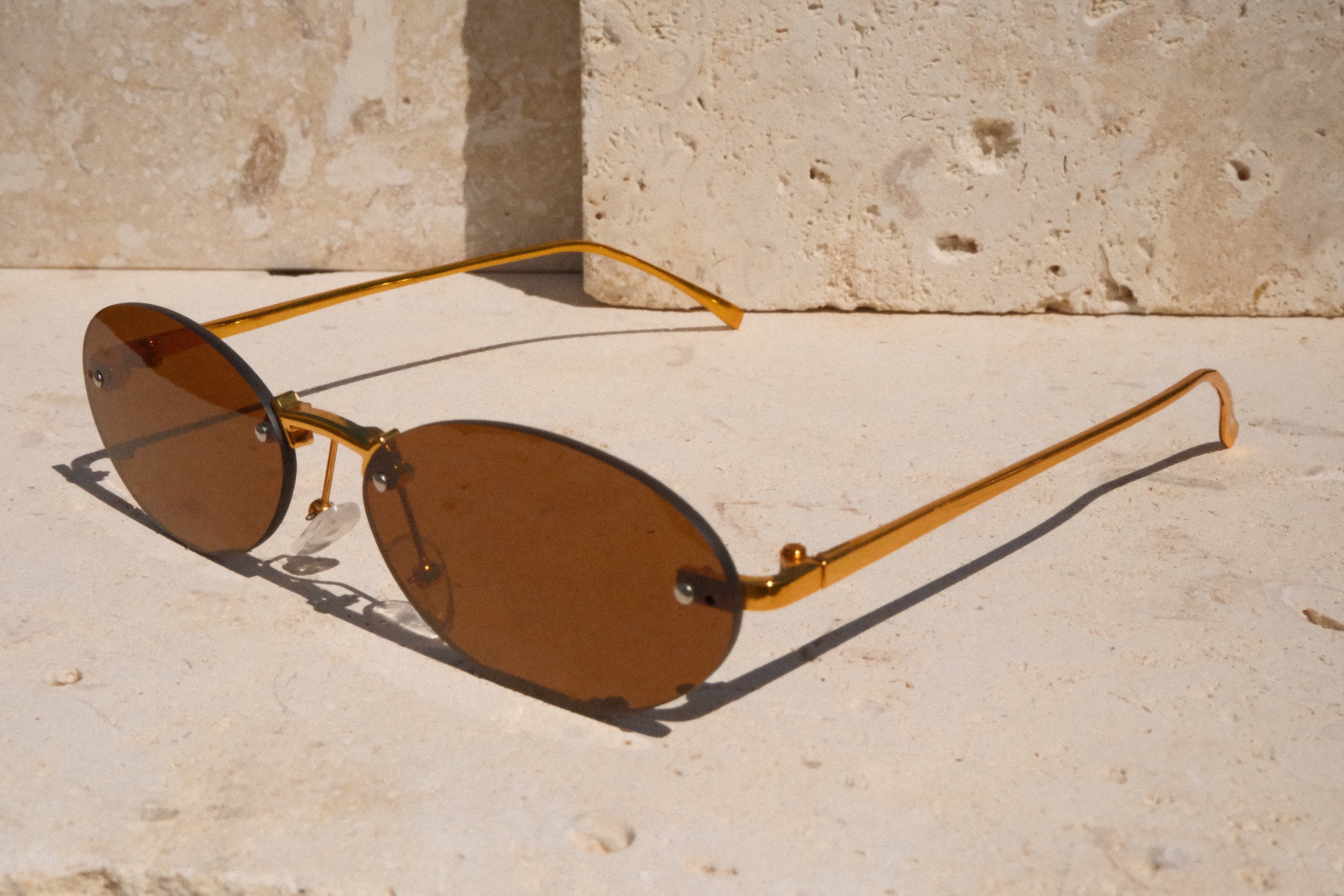 Sunglasses with gold frame and brown lenses on a stone surface