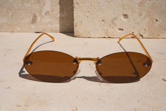 Pair of sunglasses with brown lenses and gold frames on a light stone surface.