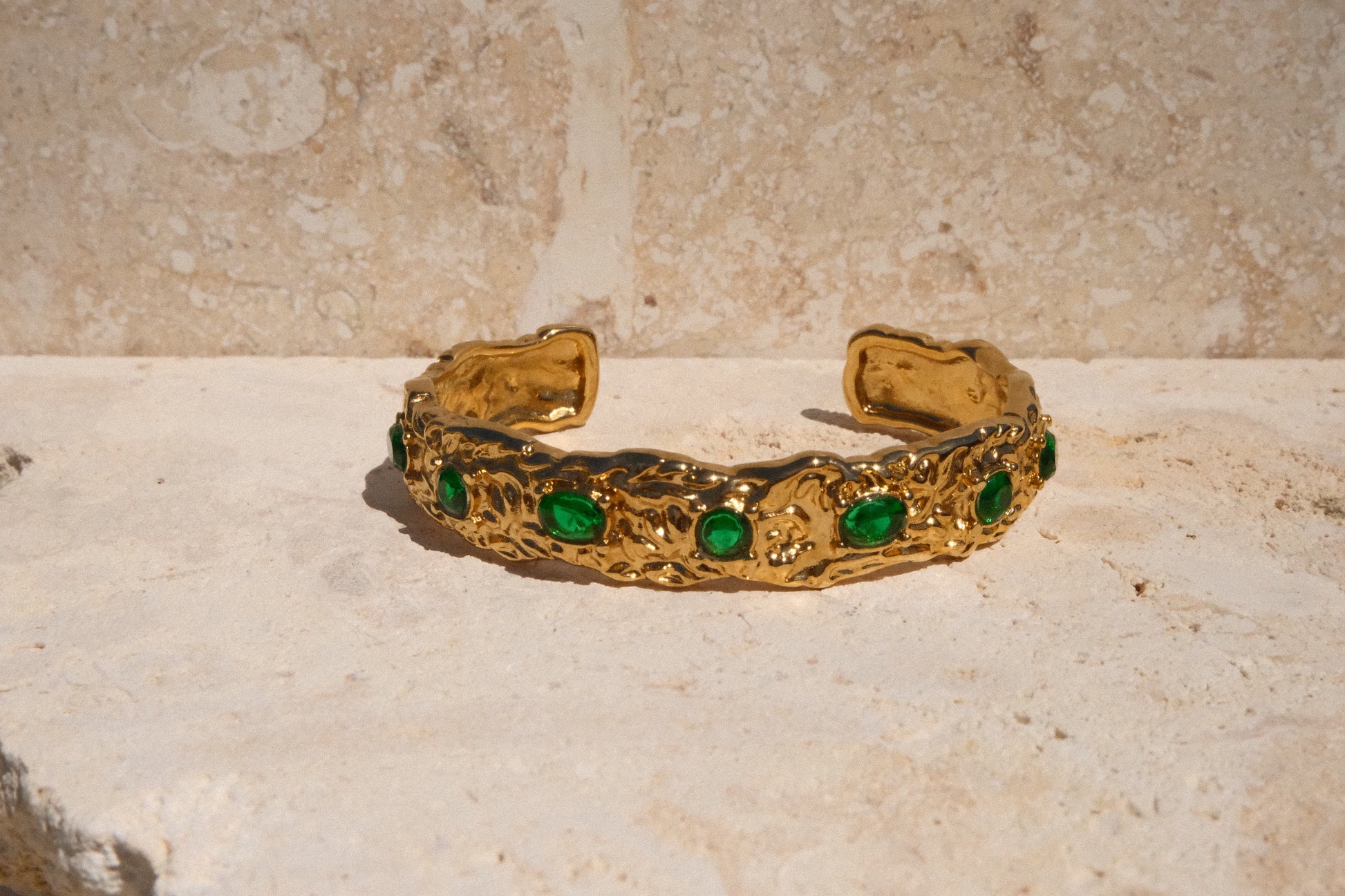 Gold bracelet with green gemstones on a stone surface