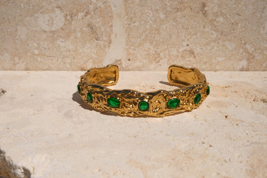 Gold bracelet with green gemstones on a stone surface