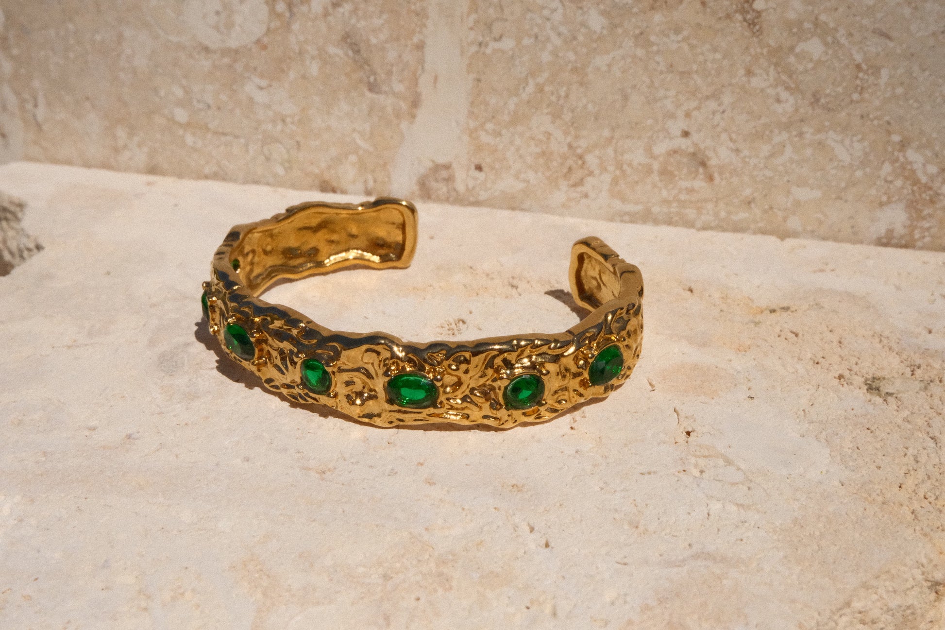 Gold bracelet with green gemstones on a textured surface