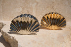 Two shell-shaped claw clips, one silver and one gold, on a stone surface.