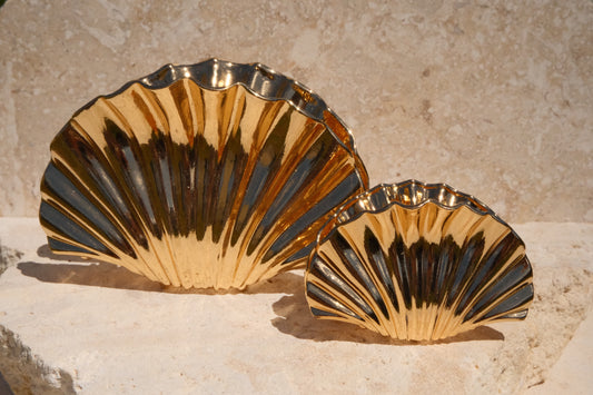 Two gold shell-shaped claw clips on a stone surface with a beige wall background.