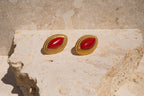 Pair of gold earrings with red stones on a stone surface