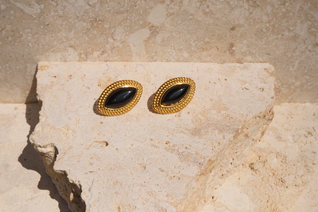 Pair of gold earrings with black stones on a beige stone surface