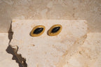 Pair of gold earrings with black stones on a beige stone surface