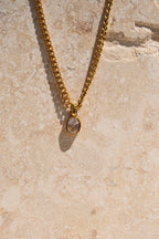 Gold necklace with a pendant on a textured beige surface
