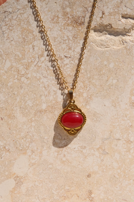 Gold necklace with a red pendant on a beige stone surface